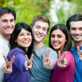 Young group of happy friends showing victory signs together outdoor in the park
